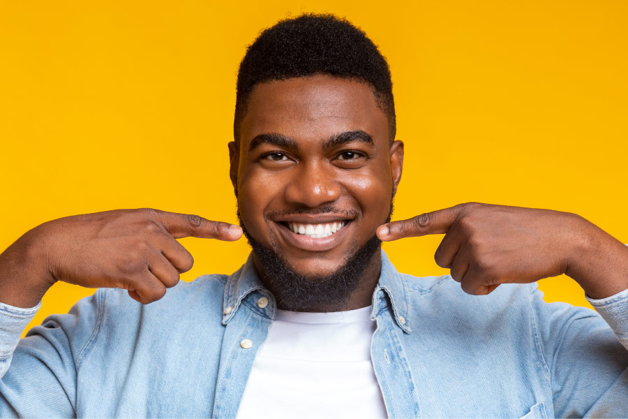 Black man smiles and points to his teeth after choosing the best professional teeth whitening treatment in Chandler, AZ