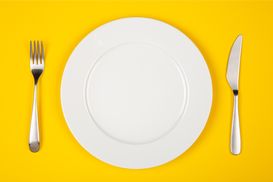 Aerial view of a white plate flanked by silverware on a yellow background