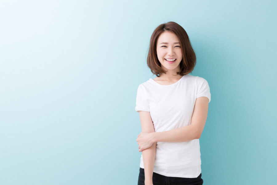 Asian woman in a white t-shirt smiles with her veneers against a blue wall