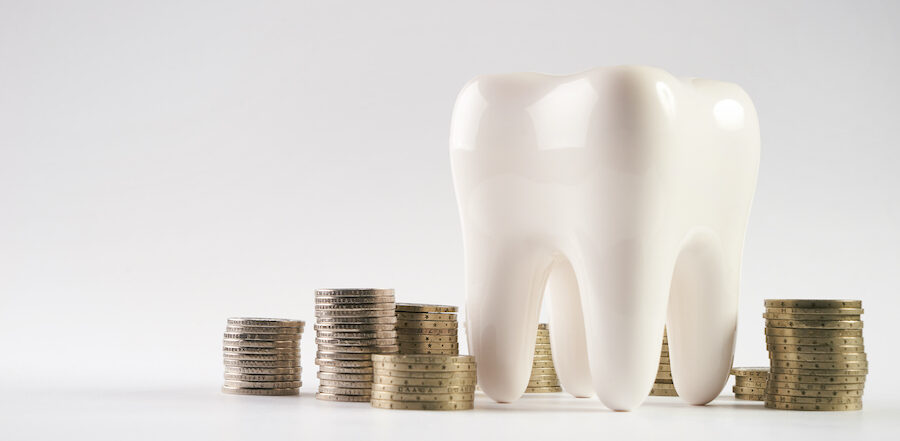 A large white tooth next to several stacks of coins to indicate savings with a dental membership plan