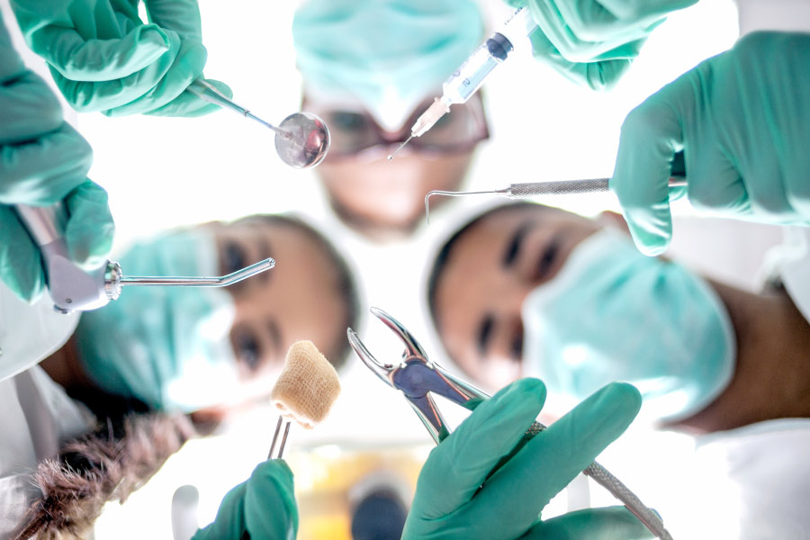 Looking up into the masked faces of dentists performing oral surgery in teal scrubs with special tools