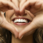 Closeup of a woman holding her hands in a heart shape in front of her smile