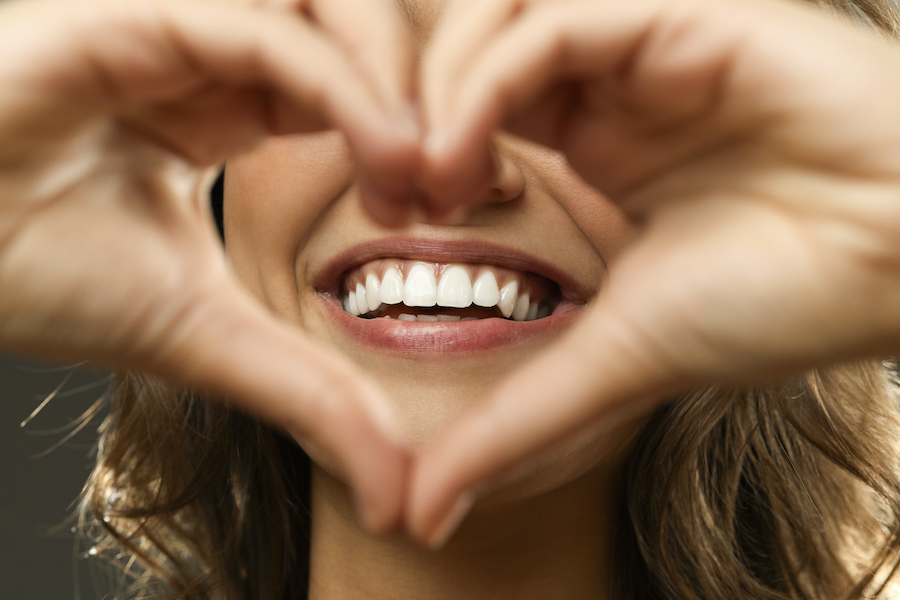 Closeup of a woman holding her hands in a heart shape in front of her smile