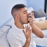 respiratory infections, respiratory infection, asthma inhaler, young man sitting on couch using an inhaler